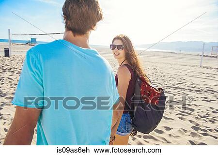 Stock Image - Young couple walking on beach, rear view. Fotosearch