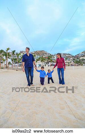 Stock Image - Young family, walking on beach, holding hands. Fotosearch