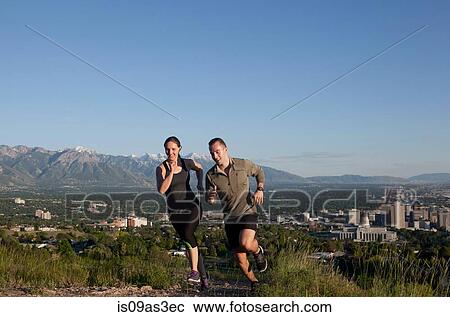 Stock Image - Young female and male runners racing along track above city in valley. Fotosearch