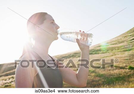 Young female runner drinking bottled water on sunlit hillside View Large Photo Image Picture - Young female runner drinking bottled water on sunlit hillside. Fotosearch