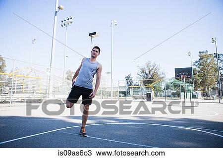 Stock Image - Young male basketball player doing warm up stretches on basketball court. Fotosearch