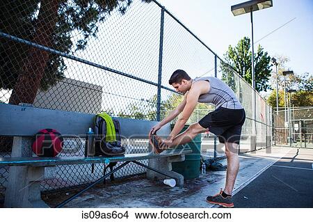 Picture - Young male basketball player stretching leg on basketball court. Fotosearch