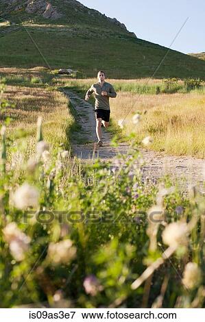 Stock Photo - Young male runner running down hillside track. Fotosearch