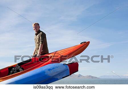 Young man carrying orange kayak, looking at camera smiling View Large Photo Image Stock Photography - Young man carrying orange kayak, looking at camera smiling. Fotosearch