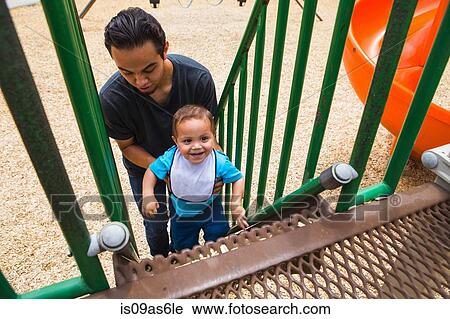 Young man guiding toddler brother up playground slide steps View Large Photo Image Stock Image - Young man guiding toddler brother up playground slide steps. Fotosearch