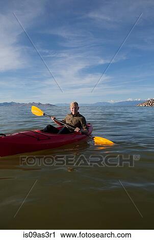 Stock Image - Young man in kayak holding paddles, looking at camera, Great Salt Lake, Utah, USA. Fotosearch