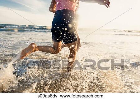 Stock Photo - Young man running in sea, low section. Fotosearch