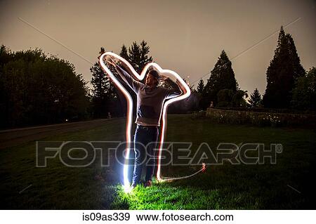 Young man, standing in field at dusk, arm in pointing position, light trail tracing body shape View Large Photo Image Stock Photo - Young man, standing in field at dusk, arm in pointing position, light trail tracing body shape. Fotosearch