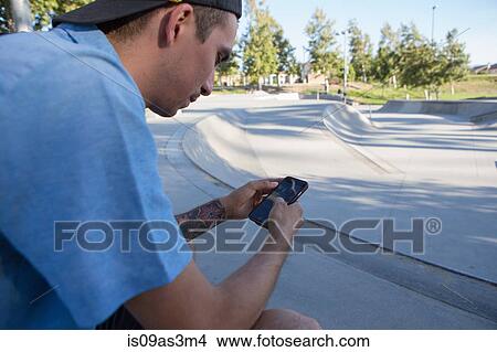 Picture - Young man using smartphone in park. Fotosearch