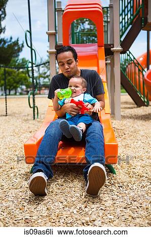 Stock Image - Young man with toddler brother on playground slide. Fotosearch