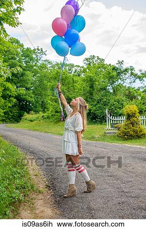 Young woman gazing up at bunch of balloons on rural road View Large Photo Image Stock Image - Young woman gazing up at bunch of balloons on rural road. Fotosearch