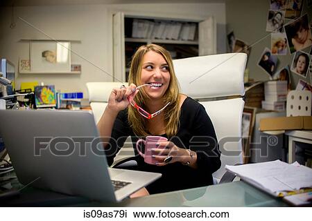Young woman in office, sitting at desk, holding eyeglasses and coffee View Large Photo Image Stock Image - Young woman in office, sitting at desk, holding eyeglasses and coffee. Fotosearch