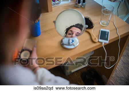 Stock Image - Young woman looking in mirror whist putting face make up on. Fotosearch