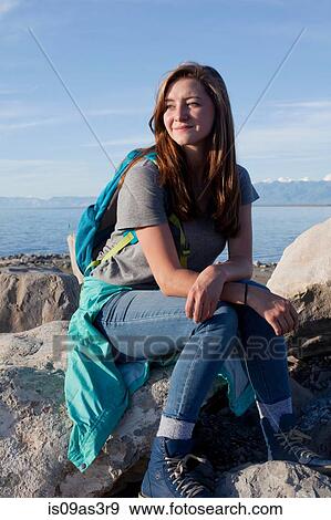 Stock Photo - Young woman sitting on rocks, leaning on elbows, looking away, Great Salt Lake, Utah, USA. Fotosearch