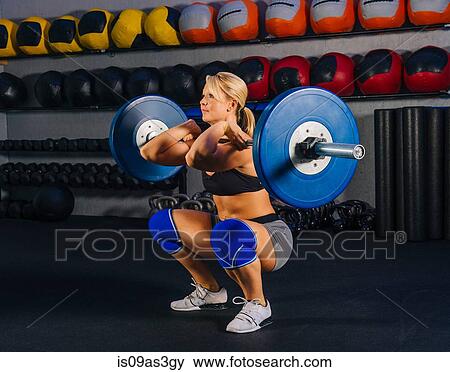 Stock Photo - Young woman squatting with barbell in gym. Fotosearch
