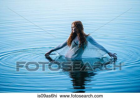 Stock Image - Young woman standing in blue lake rippling surface with her fingers. Fotosearch