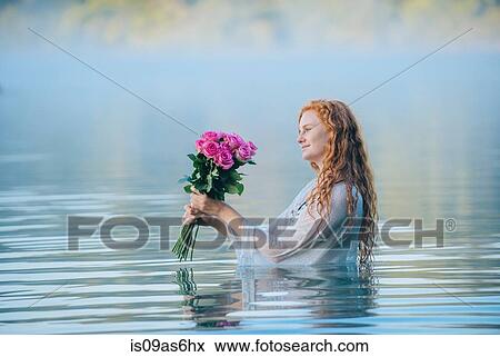 Young woman standing in lake gazing at bunch of pink roses View Large Photo Image Stock Photo - Young woman standing in lake gazing at bunch of pink roses. Fotosearch