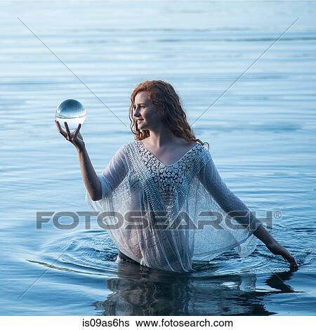 Stock Photograph - Young woman standing in lake gazing at crystal ball. Fotosearch