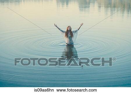 Young woman standing in middle of lake ripples with arms open View Large Photo Image Picture - Young woman standing in middle of lake ripples with arms open. Fotosearch