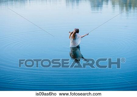 Young woman standing in middle of lake ripples with arms open and head back View Large Photo Image Picture - Young woman standing in middle of lake ripples with arms open and head back. Fotosearch