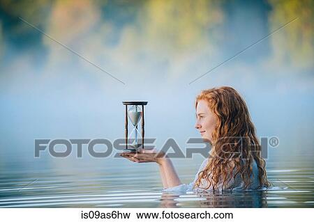 Young woman standing in misty lake gazing at hourglass View Large Photo Image Stock Photo - Young woman standing in misty lake gazing at hourglass. Fotosearch