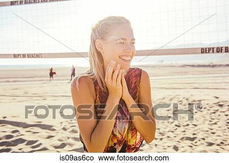 Picture - Young woman standing on beach by volleyball net, laughing. Fotosearch