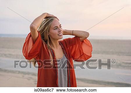 Stock Photo - Young woman standing on beach, looking at view. Fotosearch