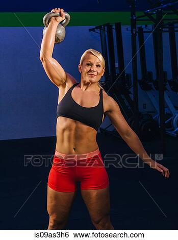 Stock Photograph - Young woman weightlifting kettlebell in gym. Fotosearch