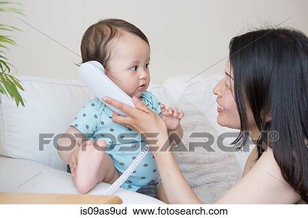 Stock Image - Baby boy and mother listening to landline telephone on sofa. Fotosearch