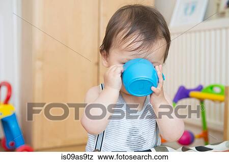 Stock Photo - Baby boy drinking from baby cup in playroom. Fotosearch