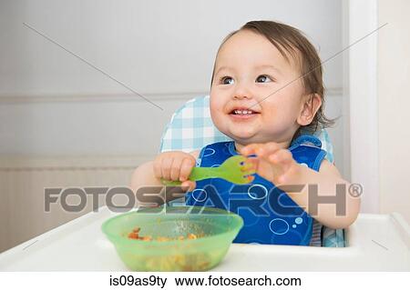 Baby boy eating baby food in kitchen high chair View Large Photo Image Stock Photo - Baby boy eating baby food in kitchen high chair. Fotosearch