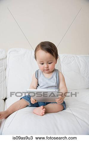 Stock Image - Baby boy sitting on sofa looking at digital tablet. Fotosearch