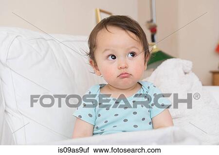 Stock Image - Baby boy sitting on sofa pulling face and looking sideways. Fotosearch