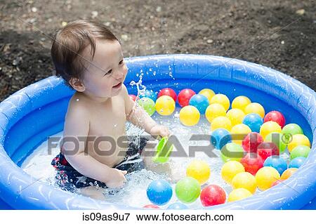 Stock Photo - Baby boy splashing in garden paddling pool. Fotosearch