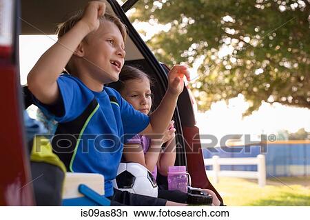 Boy and younger sister sitting in car boot watching football View Large Photo Image Picture - Boy and younger sister sitting in car boot watching football. Fotosearch