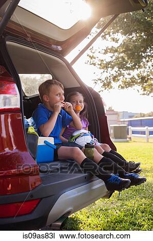Boy and younger sister sitting in car boot eating oranges on football practice break View Large Photo Image Stock Image - Boy and younger sister sitting in car boot eating oranges on football practice break. Fotosearch