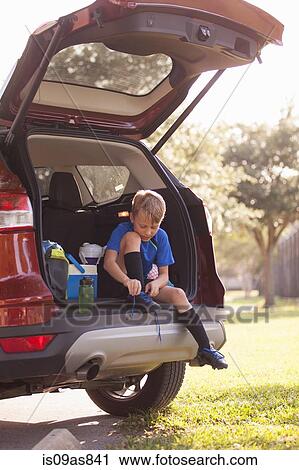 Stock Image - Boy football player sitting in car boot tying football boot laces. Fotosearch