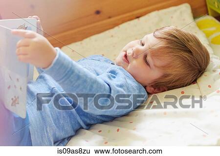 Boy lying on back in bed looking at storybook View Large Photo Image Stock Photograph - Boy lying on back in bed looking at storybook. Fotosearch