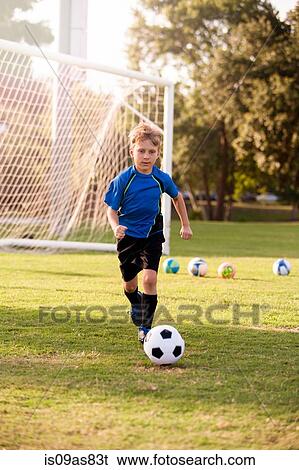 Stock Photograph - Boy running with football on practice pitch. Fotosearch