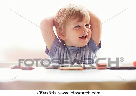 Boy sitting at table hands behind head, looking away smiling View Large Photo Image Stock Image - Boy sitting at table hands behind head, looking away smiling. Fotosearch