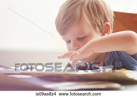 Boy sitting at table rolling crayons with finger, looking down View Large Photo Image Picture - Boy sitting at table rolling crayons with finger, looking down. Fotosearch