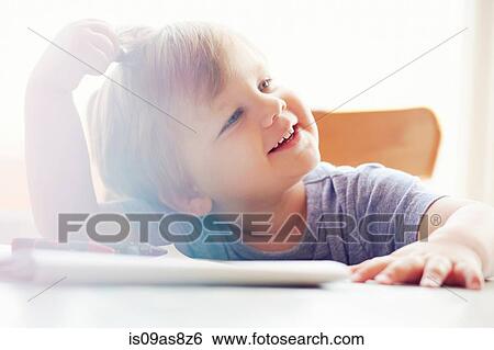 Boy sitting at table scratching head, looking away smiling View Large Photo Image Stock Photograph - Boy sitting at table scratching head, looking away smiling. Fotosearch