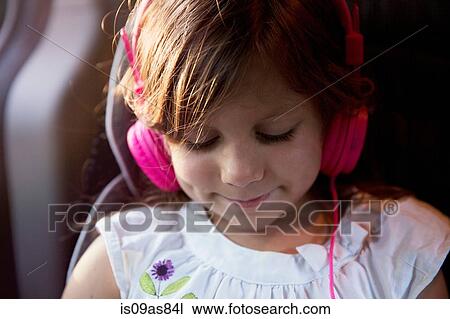 Stock Image - Close up of girl wearing pink headphones in car. Fotosearch