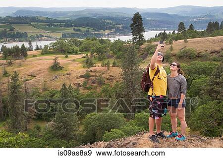 Stock Photo - Couple standing on mountain edge, taking self portrait. Fotosearch