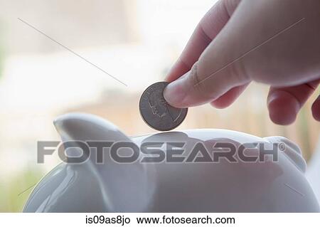 Picture - Cropped view of hand inserting coin into piggybank. Fotosearch
