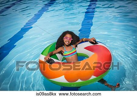 Stock Photo - Girl sitting in inflatable ring in swimming pool looking at camera smiling. Fotosearch