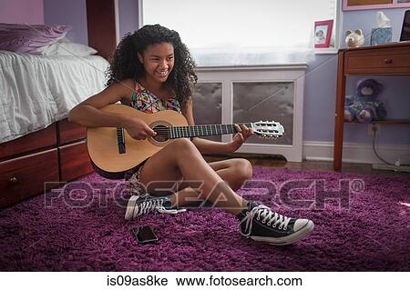 Girl sitting on bedroom floor playing guitar looking away smiling View Large Photo Image Stock Image - Girl sitting on bedroom floor playing guitar looking away smiling. Fotosearch
