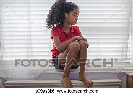 Stock Photograph - Girl sitting on windowsill looking sad, looking away. Fotosearch