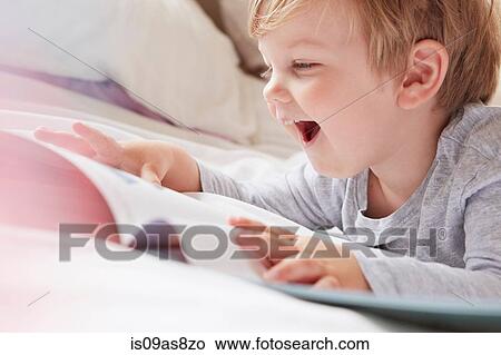 Head and shoulders of boy on bed lying on front looking at storybook, laughing View Large Photo Image Picture - Head and shoulders of boy on bed lying on front looking at storybook, laughing. Fotosearch