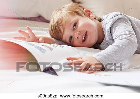 Head and shoulders of boy on bed lying on front holding storybook, looking away smiling View Large Photo Image Stock Photography - Head and shoulders of boy on bed lying on front holding storybook, looking away smiling. Fotosearch